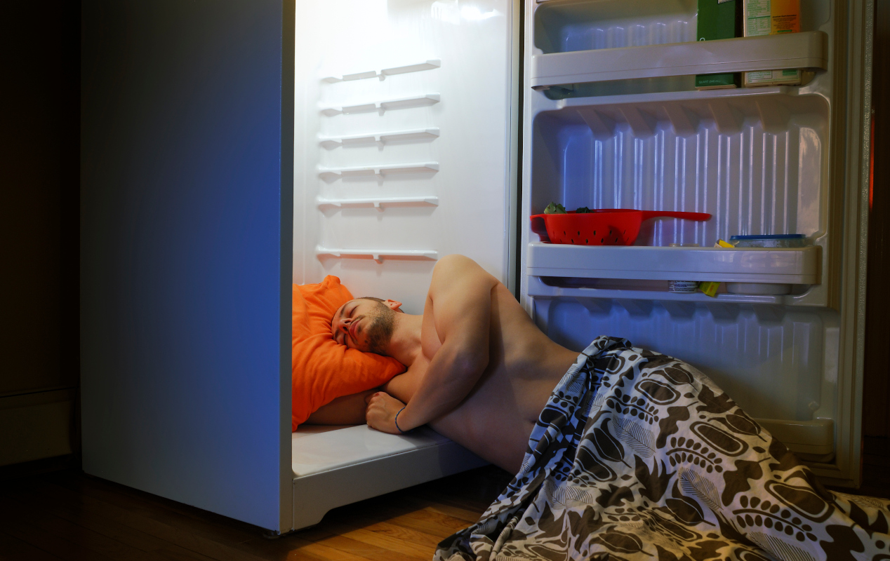 Mann legt sich mit seinem Kopf zu Abkühlung in den offenen Kühlschrank und schläft dabei ein